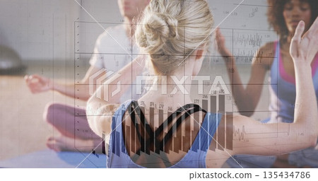 Blonde woman wearing blue top raising arms in yoga studio under soft lighting, with yoga mats Blonde woman wearing blue top raising arms in yoga studio under soft lighting, with yoga mats 135434786