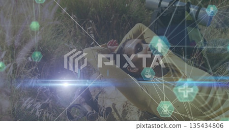 Lying female hiker resting on sloping meadow, with backpack, binoculars, lens tube, hex icons Lying female hiker resting on sloping meadow, with backpack, binoculars, lens tube, hex icons 135434806