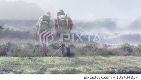Traversing hiking partners wearing jackets across coastal grassland with backpacks, mats and poles Traversing hiking partners wearing jackets across coastal grassland with backpacks, mats and poles 135434817