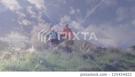Hiking mature couple walking hand in hand through wildflower meadow, with backpacks, trekking poles Hiking mature couple walking hand in hand through wildflower meadow, with backpacks, trekking poles 135434822