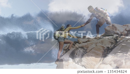 Two hikers supporting each other climbing rocky coastal cliff, with crashing waves and backpacks Two hikers supporting each other climbing rocky coastal cliff, with crashing waves and backpacks 135434824