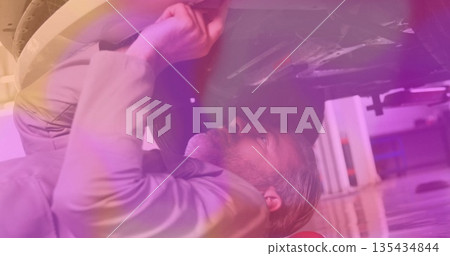 Senior mechanic wearing work shirt lying beneath vehicle in garage, with tire and creeper headrest 135434844