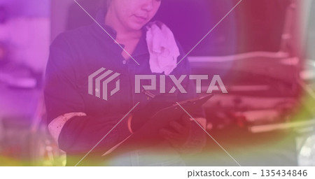 Female mechanic wearing dark coverall examining engine in auto repair shop, with clipboard and pen Female mechanic wearing dark coverall examining engine in auto repair shop, with clipboard and pen 135434846