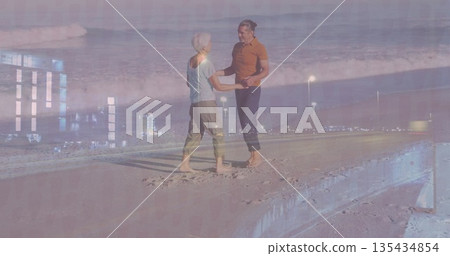 Standing barefoot couple holding hands on sandy concrete pier at dusk, with lamp posts, ocean waves 135434854