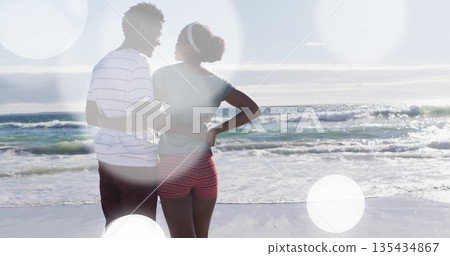 Standing African American couple embracing waists, facing calm sea at shoreline under bright sky Standing African American couple embracing waists, facing calm sea at shoreline under bright sky 135434867