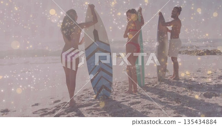 Standing friends in swimwear holding surfboards at sandy shoreline, with bright sunlight and waves 135434884