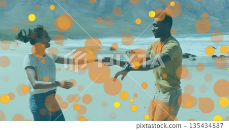 Holding hands and dancing couple on sandy shoreline next to ocean waves, with wristwatch, bokeh 135434887