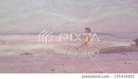 Riding barefoot woman in yellow dress along shore, with pastel pink bicycle among rocks, copy space 135434891