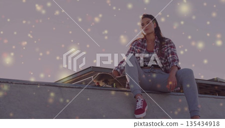 Sitting skateboarder wearing sportswear with skateboard on skatepark ramp edge and rail, copy space 135434918