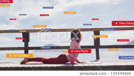 Woman wearing sportswear doing backbend on lakeside dock, with yoga mat, railing, digital banners 135434926