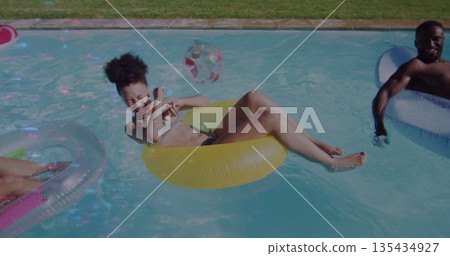 Laughing woman wearing swimsuit in yellow tube at poolside, with white tube, pink tube, beach ball Laughing woman wearing swimsuit in yellow tube at poolside, with white tube, pink tube, beach ball 135434927