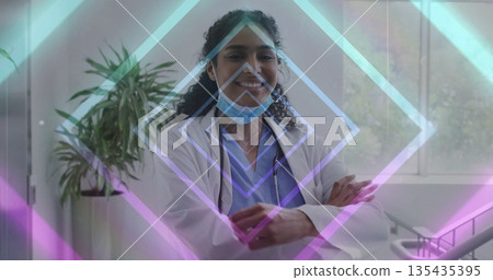 Smiling doctor crossing arms in clinic room, with stethoscope, lab coat, blue scrubs, surgical mask Smiling doctor crossing arms in clinic room, with stethoscope, lab coat, blue scrubs, surgical mask 135435395