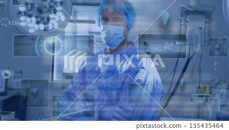 Standing surgeon in scrubs and mask crossing arms in operating room, with translucent data panels 135435464