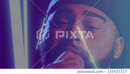 Singing bearded man wearing backward cap performing under neon tubes at concert, with microphone 135435517