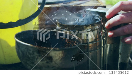 Holding beekeeper hand adjusting smoker emitting smoke at bench, with bucket, digital globe overlay Holding beekeeper hand adjusting smoker emitting smoke at bench, with bucket, digital globe overlay 135435612