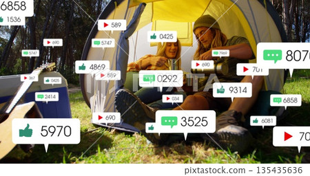 Sitting couple holding metal mugs and flask at camping tent entrance, with social icons floating Sitting couple holding metal mugs and flask at camping tent entrance, with social icons floating 135435636