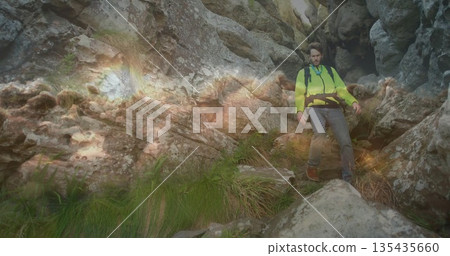 Hiker navigating gorge wearing green jacket harness belt backpack boots jagged rocks, copy space 135435660