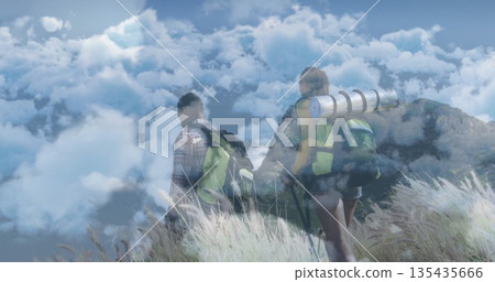 Climbing hikers navigating grassy mountain ridge under clouds, with packs, sleeping pad and poles 135435666