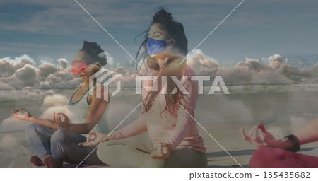 Meditating group of women cross-legged holding mudra on beach, wearing face masks and yoga mats Meditating group of women cross-legged holding mudra on beach, wearing face masks and yoga mats 135435682