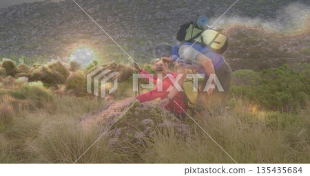 Sitting woman in red jacket holding poles with man leaning toward her on hillside with backpacks Sitting woman in red jacket holding poles with man leaning toward her on hillside with backpacks 135435684