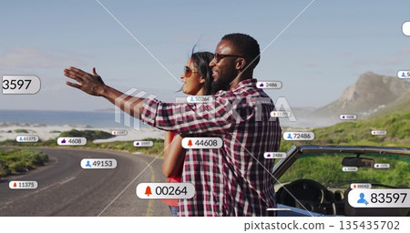 Pointing couple admiring horizon on winding coastal road, with convertible and notification icons 135435702