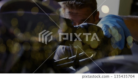 Inspecting mechanic working on motorcycle engine in garage, with blue gloves and metal components 135435704