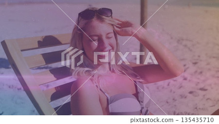 Reclining female beachgoer on lounge chair adjusting sunglasses on beach with striped bikini top Reclining female beachgoer on lounge chair adjusting sunglasses on beach with striped bikini top 135435710