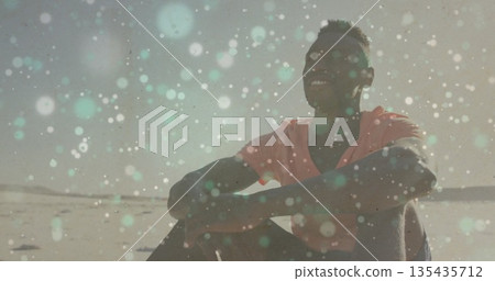 Smiling man wearing coral T-shirt and pants gazing upward on sandy beach, with bokeh lights Smiling man wearing coral T-shirt and pants gazing upward on sandy beach, with bokeh lights 135435712