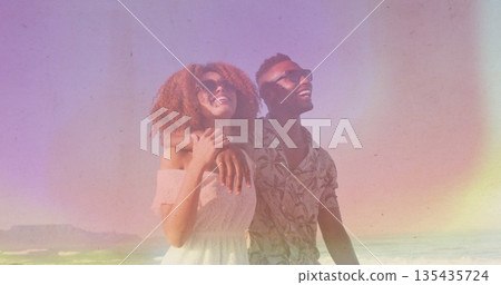Smiling couple standing on sandy shoreline, wearing sunglasses with white dress and tropical shirt Smiling couple standing on sandy shoreline, wearing sunglasses with white dress and tropical shirt 135435724