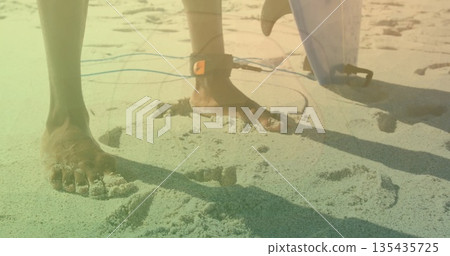 Standing barefoot surfer preparing surf session on sunlit beach, with ankle leash and surfboard fin 135435725