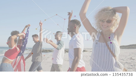 Walking five friends draping American flag and raising arms on sandy beach with rocky outcrops 135435738