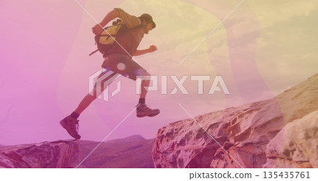 Leaping male hiker wearing baseball cap, backpack and hiking boots on desert ledges, copy space 135435761