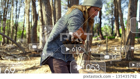 Man in grey beanie picking pine cones from stump in pine forest, with digital overlay icons Man in grey beanie picking pine cones from stump in pine forest, with digital overlay icons 135435792