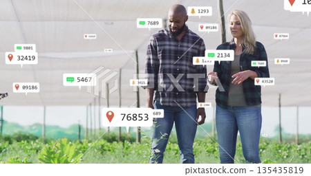 Walking two farm specialists inspecting seedling rows in shade-house, with floating analytics icons 135435819