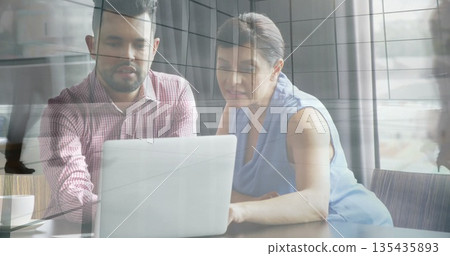 Collaborating business casual colleagues leaning at office desk by windows, laptop and coffee cup 135435893