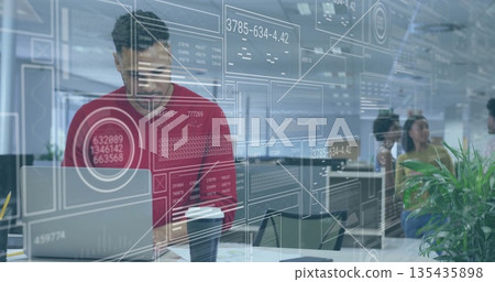 Leaning man wearing red sweater typing on laptop with coffee cup at open-plan desk, copy space 135435898