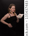 A woman in a black dress blows out a candle on a bento cake. Smoke on a black background. A girl's birthday, happiness, a gift. High quality photo 135437483