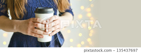 Young caucasian female holding coffee cup with fairy lights in background Young caucasian female holding coffee cup with fairy lights in background 135437697