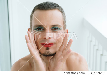 portrait of a happy feminine gay man with makeup and cosmetics on face. Transgender male with red lipstick on lips and mascara on eyes portrait of a happy feminine gay man with makeup and cosmetics on face. Transgender male with red lipstick on lips and mascara on eyes 135437698