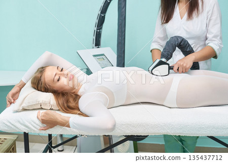 Young caucasian female undergoing non-invasive body contouring treatment 135437712
