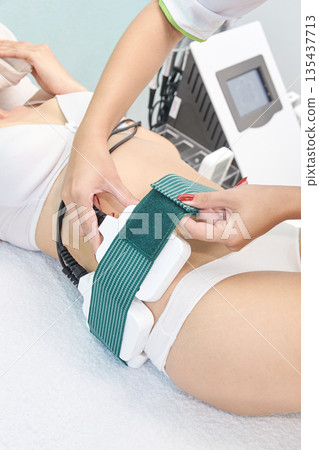 Young caucasian female undergoing non-invasive laser lipolysis procedure 135437713