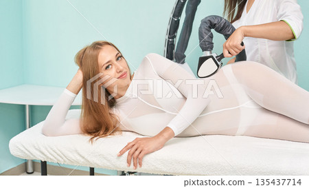 Caucasian female undergoing body sculpting treatment with technician using Caucasian female undergoing body sculpting treatment with technician using 135437714