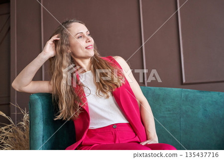 Young caucasian woman in stylish pink suit posing confidently on green sofa Young caucasian woman in stylish pink suit posing confidently on green sofa 135437716