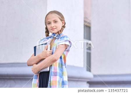 Young caucasian girl holding books in front of school building Young caucasian girl holding books in front of school building 135437721