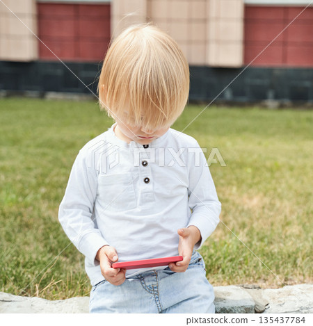 Blonde caucasian child playing with smartphone outdoors in daylight 135437784