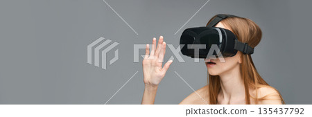 Young caucasian female engaged with virtual reality headset on gray background 135437792