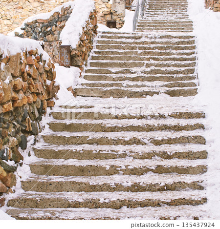 Snow-covered stone steps leading upward with rustic brick walls in winter Snow-covered stone steps leading upward with rustic brick walls in winter 135437924