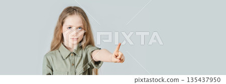 Caucasian young girl pointing forward with serious expression in green shirt 135437950