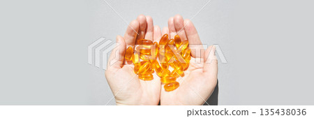 Hands holding golden fish oil capsules against neutral background for health 135438036