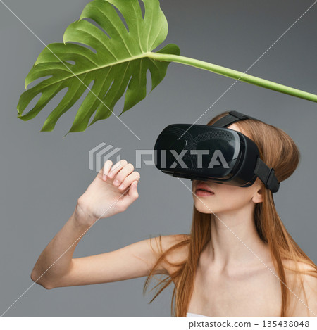 Young caucasian female engaging in vr experience with giant leaf against gray Young caucasian female engaging in vr experience with giant leaf against gray 135438048